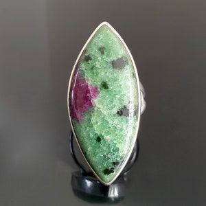 May include: A silver ring featuring a green and pink gemstone. The gemstone is teardrop shaped and has a mottled pattern.