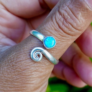 May include: A silver ring featuring a blue opal stone and a spiral design. The ring is adjustable and can be worn on any finger.