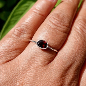 May include: A silver ring with a red oval gemstone. The ring is on a person's finger.