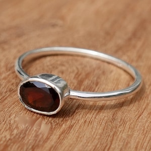 May include: A silver ring with a dark red oval gemstone.