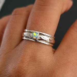 Peut inclure: Une bague en argent avec trois bandes et une petite pierre d'opale irisée au centre.