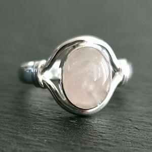 Op de afbeelding: Een zilveren ring met een delicaat ontwerp met een ovale, lichtroze edelsteen.