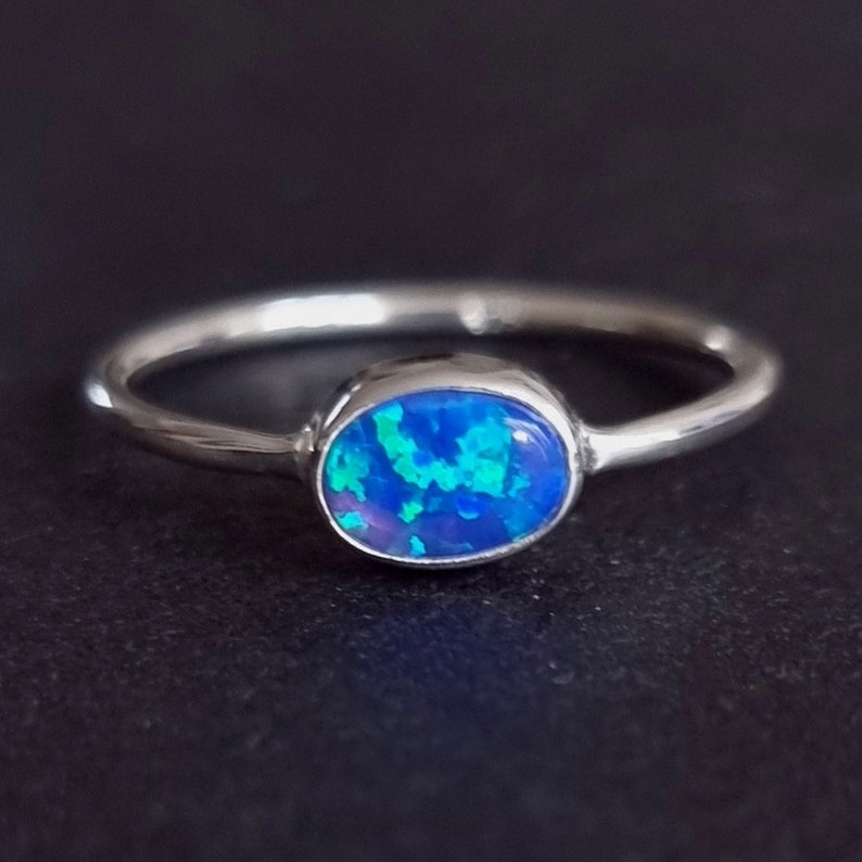 May include: A silver ring with a blue opal gemstone. The opal has a blue, green, and purple iridescent sheen.