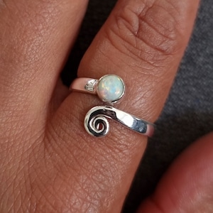 May include: A silver ring featuring a white opal gemstone and a swirl design.
