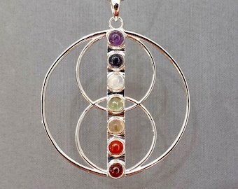 May include: A silver-toned pendant necklace featuring a vertical bar set with seven small, round, multi-colored gemstones in shades of purple, dark blue, white, light green, yellow, orange, and red, framed by two interlocking silver circles.