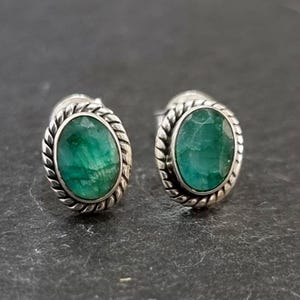 May include: A pair of silver earrings with oval-shaped green gemstones set in a twisted silver frame.
