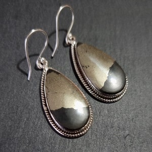 May include: A pair of silver dangle earrings featuring teardrop-shaped pyrite stones. The stones are a combination of gold and black.