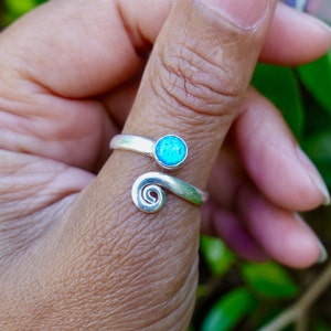 Pode incluir: Um anel de polegar de prata com uma pedra de opala azul. O anel é desenhado com um detalhe em espiral.