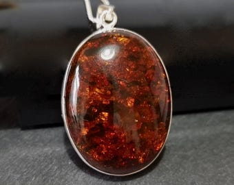 May include: A silver pendant with a large oval-shaped amber stone. The amber is a deep reddish-brown color with flecks of gold throughout.