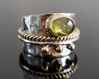 May include: A silver and gold ring with a green gemstone. The ring has a hammered texture and a rope-like design around the band.