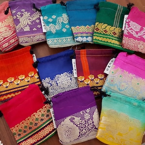 May include: Assortment of colorful drawstring pouches with intricate patterns and gold accents. The pouches are made of fabric and have a drawstring closure. The pouches are labeled with the word "Gems".