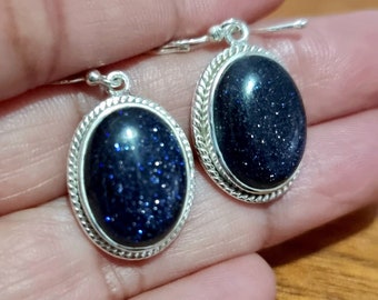 May include: A pair of silver earrings with oval-shaped blue gemstone stones. The stones have a sparkly, speckled appearance.
