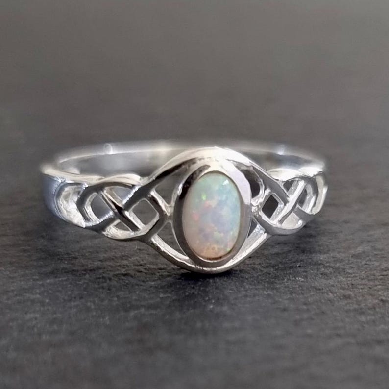 May include: A silver ring with a white opal stone set in a Celtic knot design.