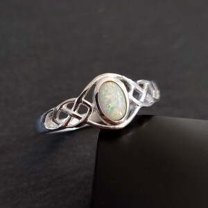 May include: A silver ring with a white opal gemstone set in a Celtic knot design.