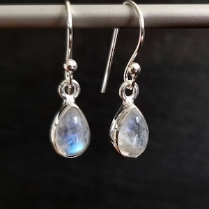 May include: A pair of silver teardrop earrings with moonstone gemstones. The earrings have a simple design and are perfect for everyday wear.