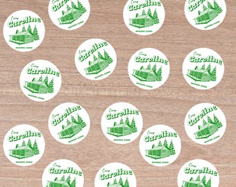 May include: A collection of round white stickers with a green illustration of a cabin and trees. The text "Camp Caroline" is arched above the cabin, with "Breckenridge, Colorado" below.