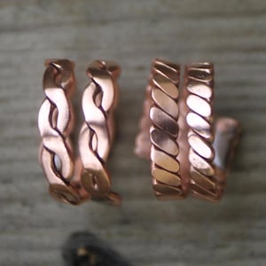 May include: Three copper rings, two with a braided design and one with a ridged design. The rings are stacked together.