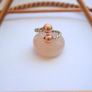 Handmade twisted copper and brass open ring with smooth ball ends, displayed on a clear quartz crystal.