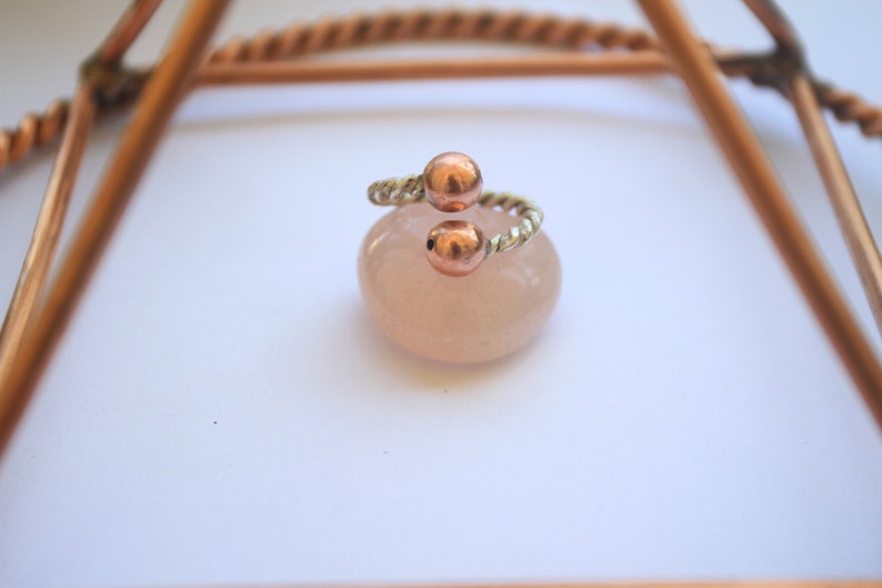 Handmade twisted copper and brass open ring with smooth ball ends, displayed on a clear quartz crystal.