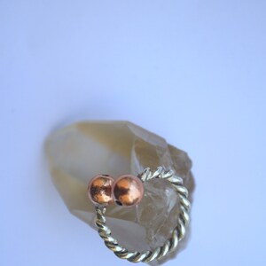 Handmade twisted copper and brass open ring with smooth ball ends, displayed on a clear quartz crystal.