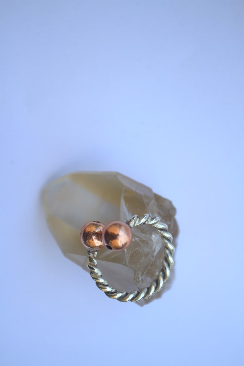 Handmade twisted copper and brass open ring with smooth ball ends, displayed on a clear quartz crystal.