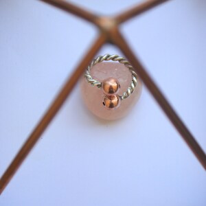 Handmade twisted copper and brass open ring with smooth ball ends, displayed on a clear quartz crystal.