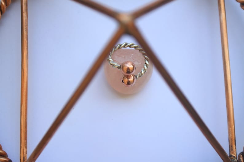 Handmade twisted copper and brass open ring with smooth ball ends, displayed on a clear quartz crystal.