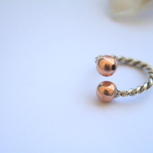Handmade twisted copper and brass open ring with smooth ball ends, displayed on a clear quartz crystal.