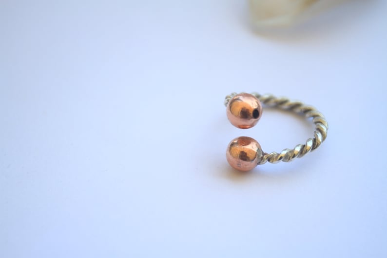Handmade twisted copper and brass open ring with smooth ball ends, displayed on a clear quartz crystal.