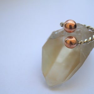 Handmade twisted copper and brass open ring with smooth ball ends, displayed on a clear quartz crystal.
