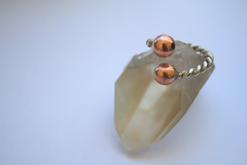Handmade twisted copper and brass open ring with smooth ball ends, displayed on a clear quartz crystal.