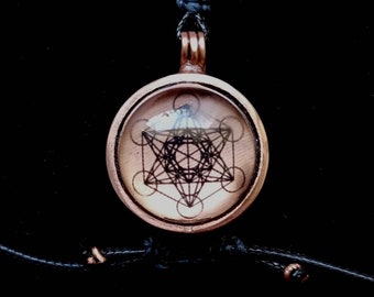 May include: A copper pendant necklace with a black cord. The pendant features a clear glass dome with a black and white geometric design inside.