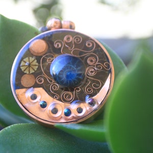 May include: A copper pendant featuring a blue and black swirl design, encircled by copper wire and small copper beads.