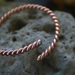 May include: A copper wire bracelet with a twisted design. The bracelet is open and has a gap where the ends meet.