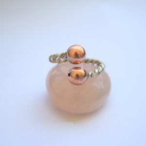 Handmade twisted copper and brass open ring with smooth ball ends, displayed on a clear quartz crystal.