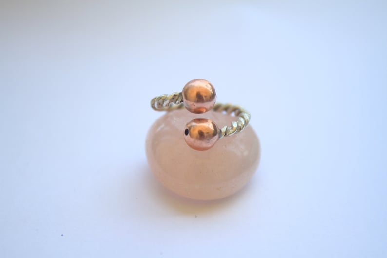 Handmade twisted copper and brass open ring with smooth ball ends, displayed on a clear quartz crystal.
