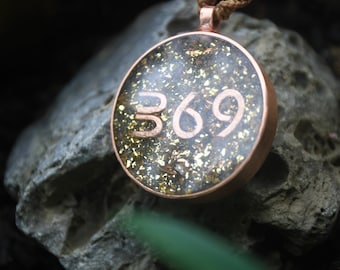 May include: A copper pendant with a clear resin coating and gold flecks. The number 369 is visible inside the resin.