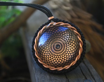 May include: A copper and black pendant necklace with a geometric design. The pendant features a circular copper frame with a black and gold geometric pattern inside.