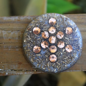May include: A round, clear resin orb with a copper-colored geometric pattern embedded inside. The orb is set on a wooden surface.
