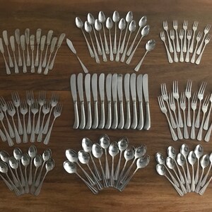 May include: A set of silverware, including spoons, forks, and knives, arranged in rows on a wooden surface. The silverware is made of polished stainless steel.