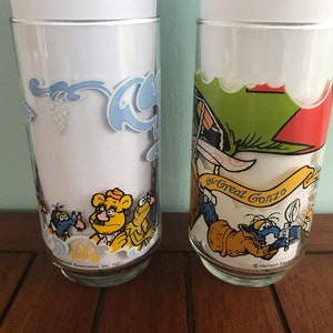 May include: Two vintage glass drinking glasses with colorful cartoon characters. The first glass features a yellow bear with a mustache and a blue bird. The second glass features a blue bird with a red hat and the text "The Great Gonzo".