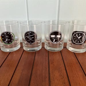 May include: Four clear glass tumblers with black and white airplane instrument designs. The designs include a compass, an altimeter, a speed indicator, and a heading indicator.
