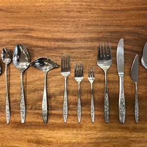May include: A set of silver cutlery with floral designs on the handles. The set includes a butter knife, a dinner knife, a dinner fork, a salad fork, a teaspoon, a soup spoon, a serving spoon, and a cake server.