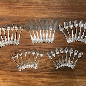 May include: A set of silver flatware, including forks, knives, and spoons. The flatware is arranged in rows on a wooden surface.