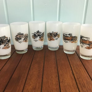 May include: Set of six white frosted glass tumblers with vintage car illustrations. Each glass features a different car model with the name of the car and the year printed below the image.