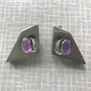 May include: A pair of silver earrings with geometric shapes and purple amethyst stones.