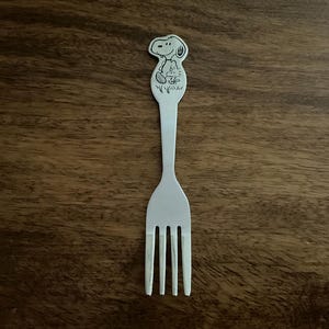 May include: White plastic fork with a black and white cartoon image of Snoopy on the handle.