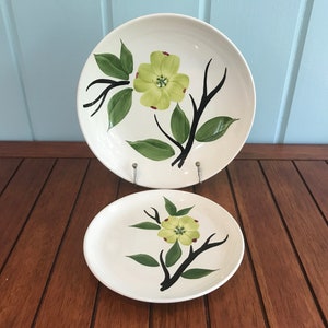 May include: Two white ceramic plates with a floral design. The larger plate has a yellow flower with green leaves and black branches. The smaller plate has a similar design.