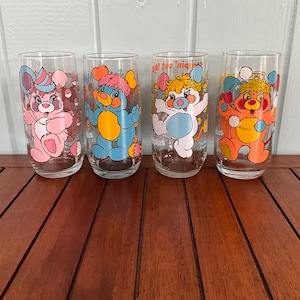 May include: Set of four clear drinking glasses with cartoon bear illustrations in pink, blue, white, and orange. Each glass features a different bear design with the text "Happy Apples".
