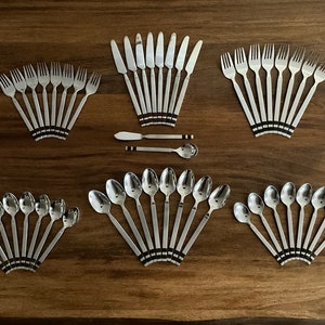 May include: A set of silverware with black and white stripes on the handles. The set includes forks, knives, spoons, and a butter knife. The silverware is arranged in a fan shape on a wooden surface.